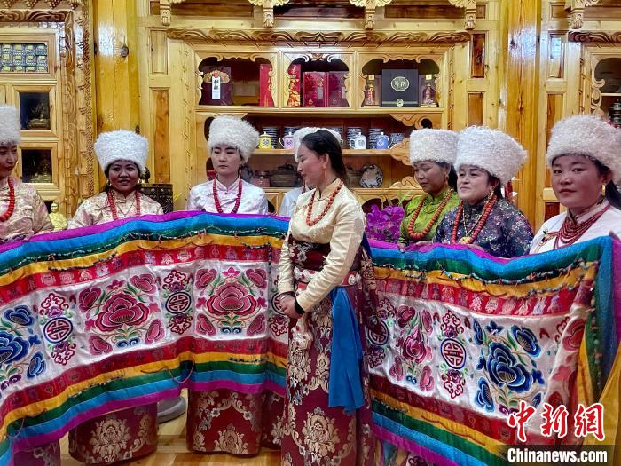 圖為女性展示村民自發(fā)繡制的“百米五彩哈達(dá)”?！±钣穹?攝